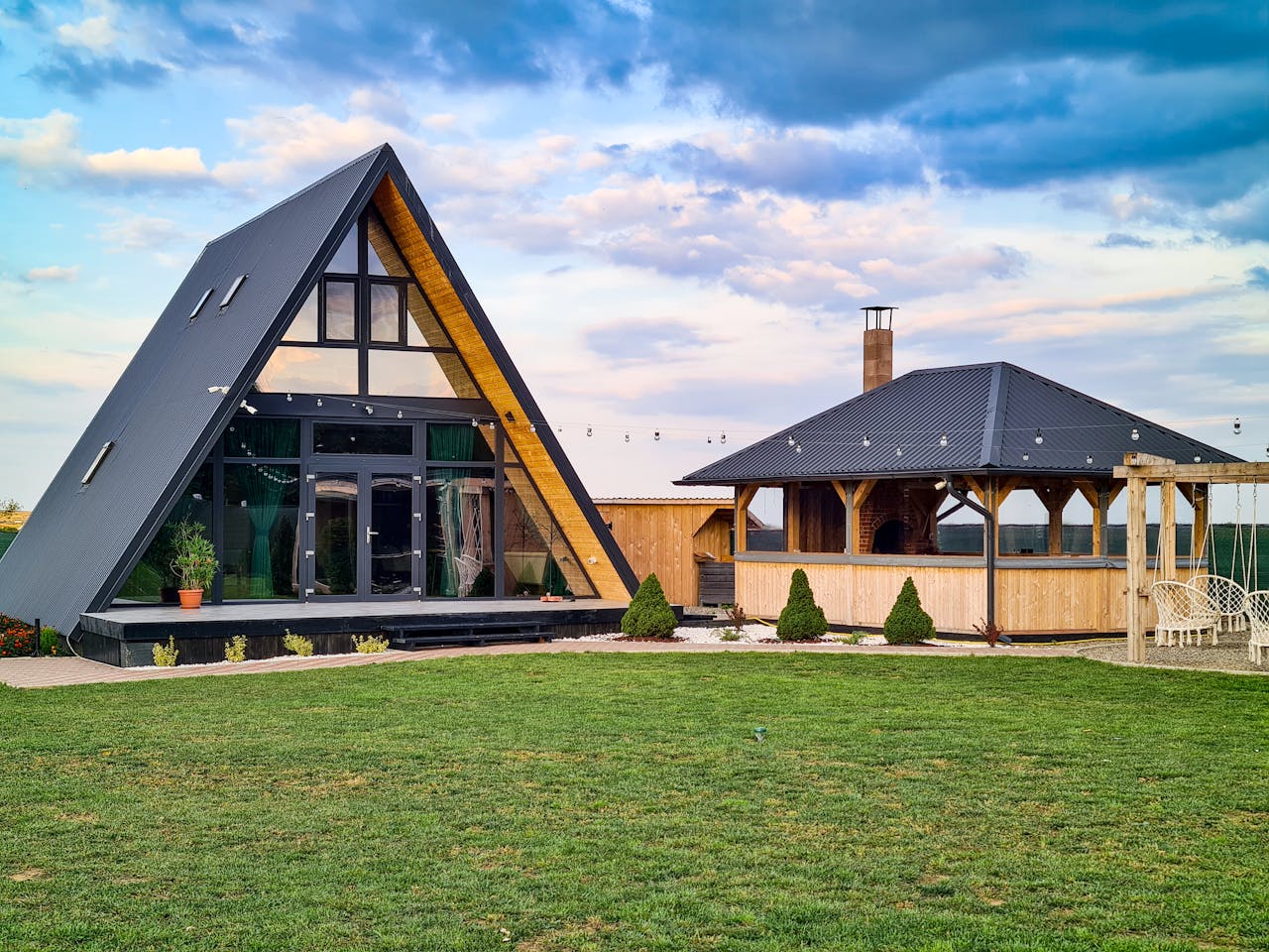 Stylish A-frame cabin and wooden gazebo in a lush summer setting, perfect for vacation retreats.